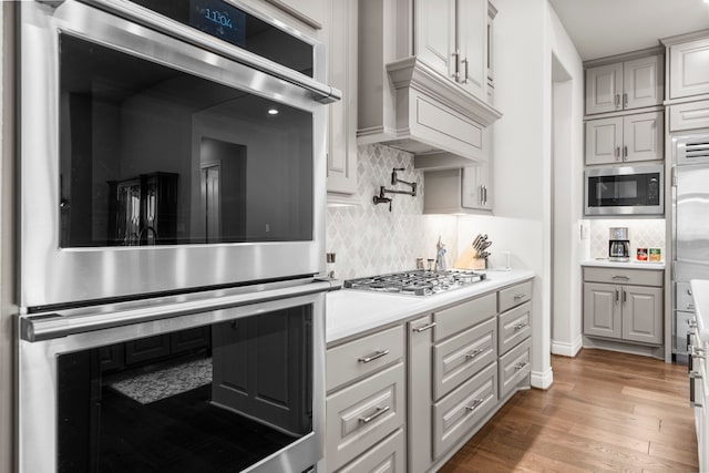 28911 Ally Lynn Way, Katy, TX 77494 - kitchen with appliances with stainless steel finishes, light countertops, tasteful backsplash, wood finished floors, and custom exhaust hood