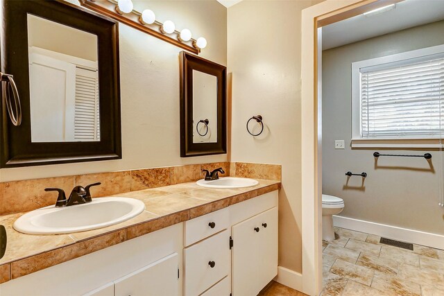 1200 E US Highway 90, Flatonia, TX 78941 - bathroom featuring baseboards, double vanity, stone finish flooring, and toilet