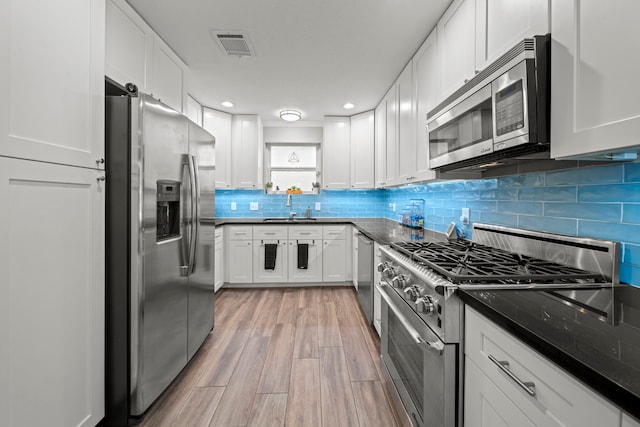 3010 Helberg Rd, Houston, TX 77092 - kitchen with appliances with stainless steel finishes, a sink, dark countertops, light wood-style floors, and white cabinets