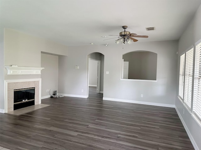 15318 Griggs Point Ln, Sugar Land, TX 77498 - unfurnished living room with a ceiling fan, dark wood-style flooring, a tiled fireplace, arched walkways, and baseboards
