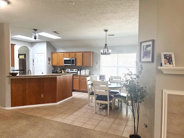 7126 Leens Lodge Ln, Humble, TX 77346 - kitchen featuring appliances with stainless steel finishes, light tile patterned floors, a textured ceiling, brown cabinets, and pendant lighting
