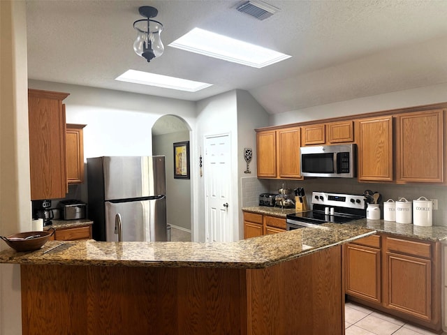 7126 Leens Lodge Ln, Humble, TX 77346 - kitchen with stainless steel appliances, a skylight, brown cabinetry, lofted ceiling, and dark stone countertops