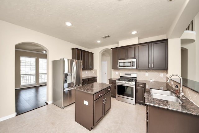 2304 Shadow Canyon Ct, Pearland, TX 77584 - kitchen with appliances with stainless steel finishes, arched walkways, a sink, dark stone counters, and recessed lighting