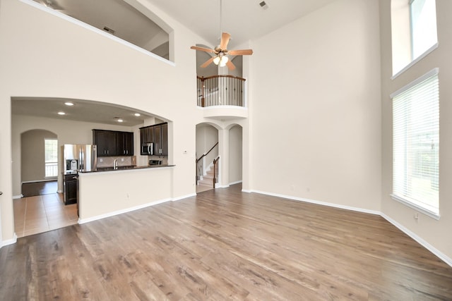 2304 Shadow Canyon Ct, Pearland, TX 77584 - unfurnished living room with a ceiling fan, a high ceiling, arched walkways, light wood finished floors, and baseboards