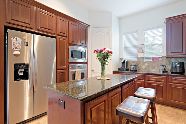 19406 Egret Haven Ln, Cypress, TX 77433 - kitchen featuring stainless steel appliances, light tile patterned floors, a center island, backsplash, and dark stone countertops