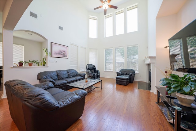 19406 Egret Haven Ln, Cypress, TX 77433 - living room featuring a ceiling fan, wood-type flooring, a towering ceiling, a fireplace with flush hearth, and arched walkways
