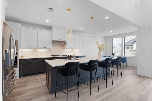 4706 Oak Glen Ct, Manvel, TX 77578 - kitchen featuring stainless steel fridge with ice dispenser, light countertops, decorative backsplash, a kitchen island with sink, and light wood-style floors