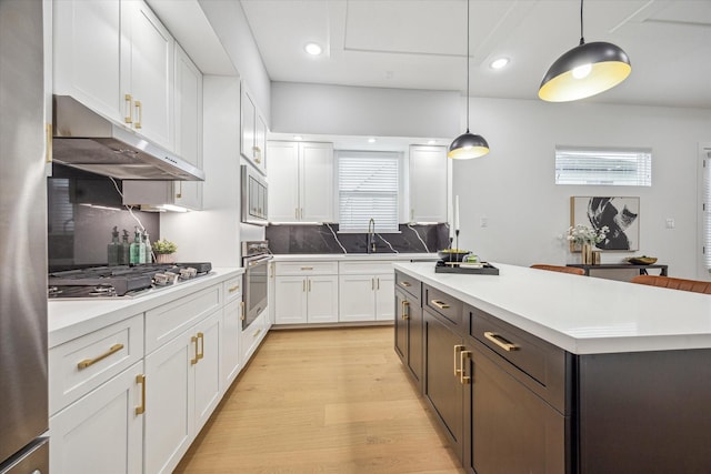 2110 Beall St, Houston, TX 77008 - kitchen featuring under cabinet range hood, stainless steel appliances, white cabinetry, light wood-style floors, and a kitchen island