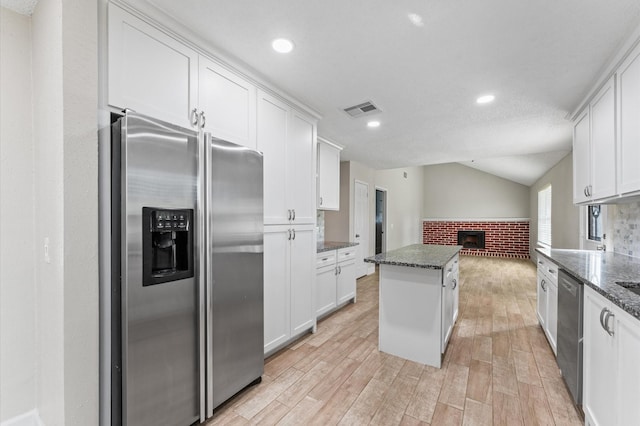 4519 Pioneer Trl, Sugar Land, TX 77479 - kitchen featuring appliances with stainless steel finishes, a fireplace, light wood finished floors, a kitchen island, and white cabinets