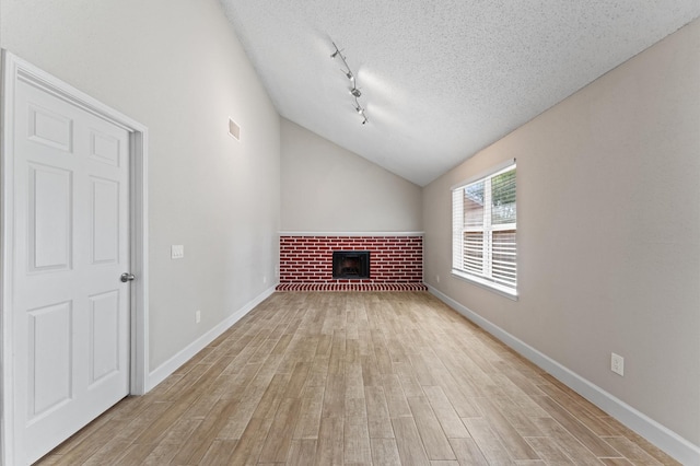 4519 Pioneer Trl, Sugar Land, TX 77479 - unfurnished living room featuring a textured ceiling, light wood-style flooring, a brick fireplace, baseboards, and lofted ceiling