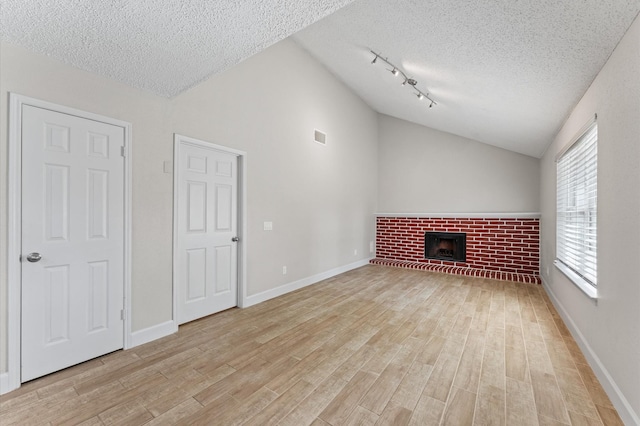 4519 Pioneer Trl, Sugar Land, TX 77479 - unfurnished living room with a textured ceiling, lofted ceiling, light wood-style flooring, a brick fireplace, and baseboards