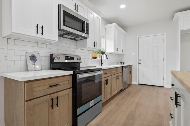 2811 Winbern St, Houston, TX 77004 - kitchen featuring appliances with stainless steel finishes, light wood-style floors, a sink, tasteful backsplash, and white cabinetry