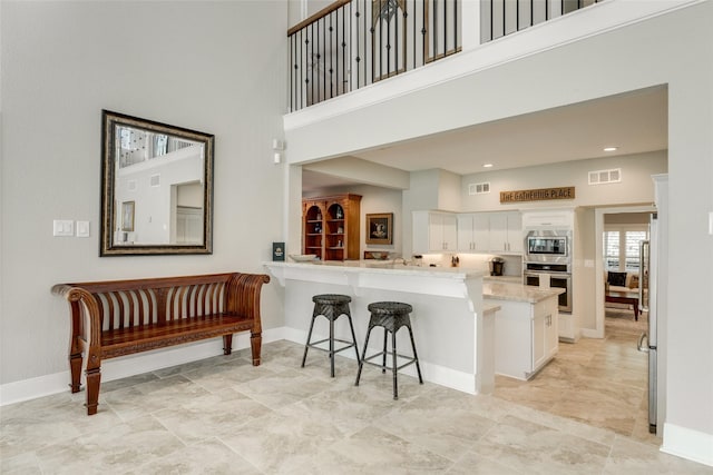 14001/14009 W Hughes Rd, Dickinson, TX 77539 - kitchen with appliances with stainless steel finishes, a towering ceiling, white cabinetry, a breakfast bar, and baseboards