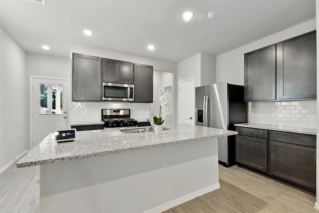 25707 Hickory Pecan Trl, Tomball, TX 77375 - kitchen with stainless steel appliances, a sink, backsplash, light stone counters, and light wood-style flooring