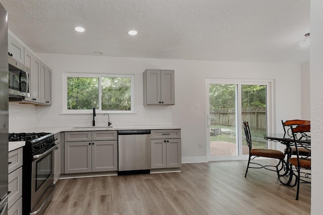 3 Meadow Beauty, The Woodlands, TX 77381 - kitchen featuring appliances with stainless steel finishes, a sink, gray cabinets, a textured ceiling, and light wood-type flooring