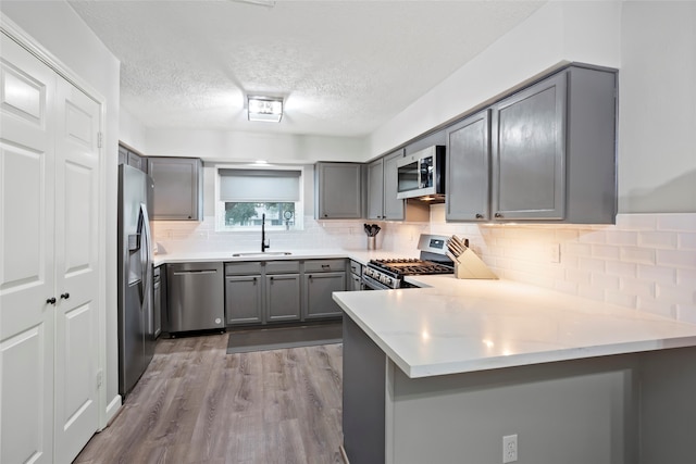654 W Country Grove Cir, Pearland, TX 77584 - kitchen with stainless steel appliances, a sink, gray cabinets, a peninsula, and wood finished floors