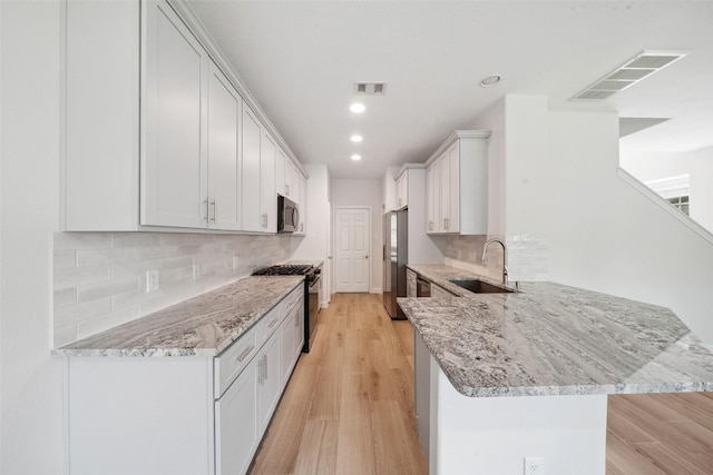 10 Fairlee Ct, The Woodlands, TX 77354 - kitchen with stainless steel appliances, a sink, a peninsula, light stone counters, and white cabinetry