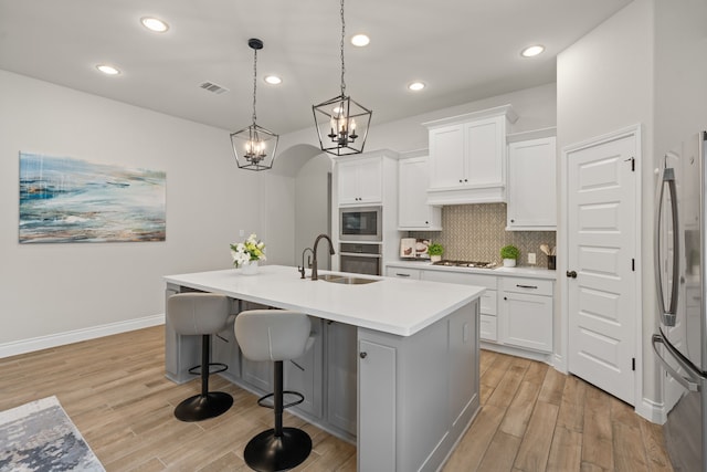 2915 Finch Ct, Katy, TX 77493 - kitchen with stainless steel appliances, a sink, light wood-style floors, an island with sink, and backsplash