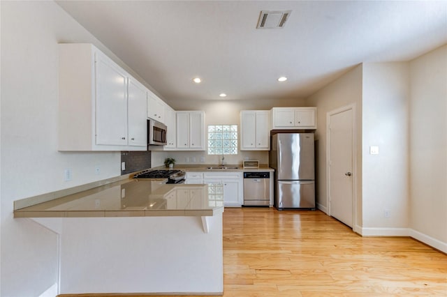 3721 Main Poplar Dr, Houston, TX 77025 - kitchen with appliances with stainless steel finishes, a sink, light wood-type flooring, white cabinetry, and recessed lighting