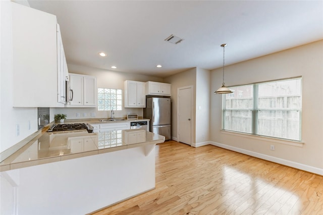 3721 Main Poplar Dr, Houston, TX 77025 - kitchen with stainless steel appliances, a sink, a peninsula, white cabinets, and light wood-type flooring