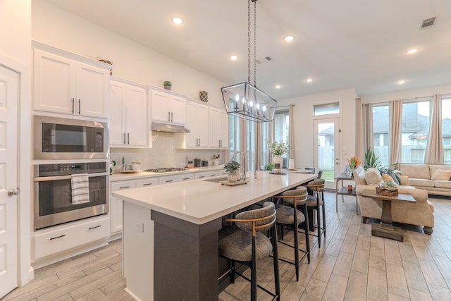 30707 Thicket Ct, Fulshear, TX 77441 - kitchen with appliances with stainless steel finishes, light wood-type flooring, an island with sink, light countertops, and white cabinetry