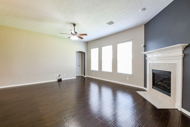 18002 Outback Lakes Trl, Humble, TX 77346 - unfurnished living room with a ceiling fan, a tiled fireplace, dark wood-type flooring, arched walkways, and baseboards