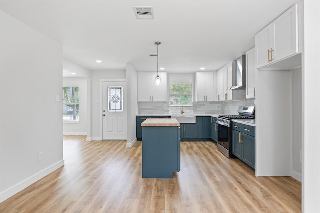 5115 Clay St, Houston, TX 77023 - kitchen with stainless steel gas range, wood counters, wall chimney exhaust hood, white cabinets, and recessed lighting
