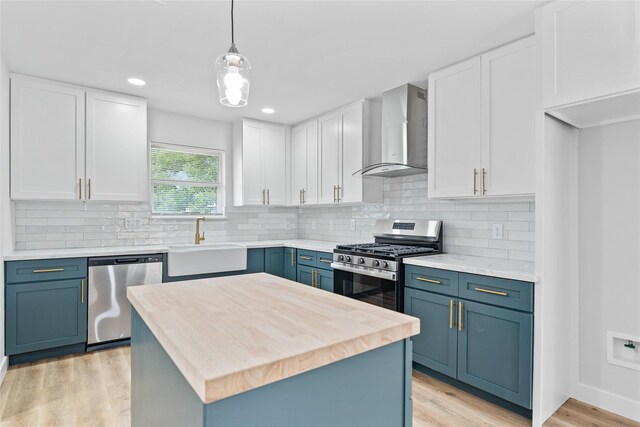 5115 Clay St, Houston, TX 77023 - kitchen featuring appliances with stainless steel finishes, wall chimney range hood, a sink, light wood-style floors, and white cabinets