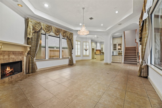16610 Champagne Falls Ct, Spring, TX 77379 - unfurnished living room with a tiled fireplace, a raised ceiling, stairway, tile patterned floors, and a chandelier