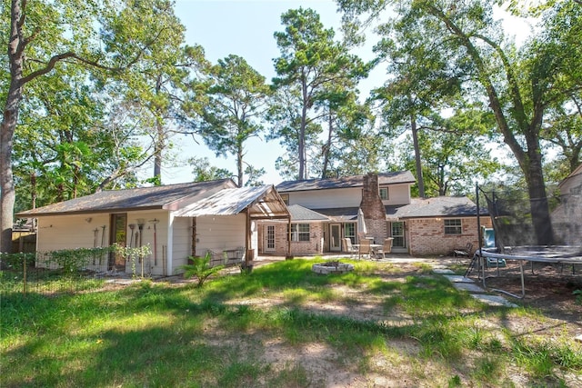 676 Ravensworth Dr, Conroe, TX 77302 - back of property featuring a trampoline, a patio area, brick siding, and a yard