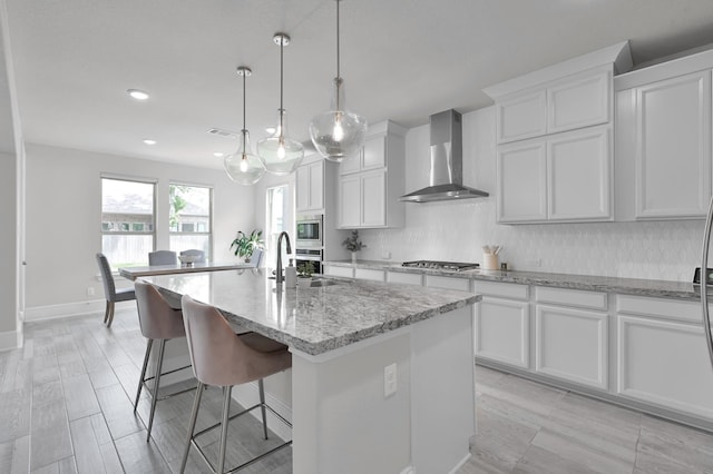 503 Woodsy Pine Ct, Conroe, TX 77304 - kitchen with wall chimney range hood, stainless steel appliances, a sink, tasteful backsplash, and an island with sink