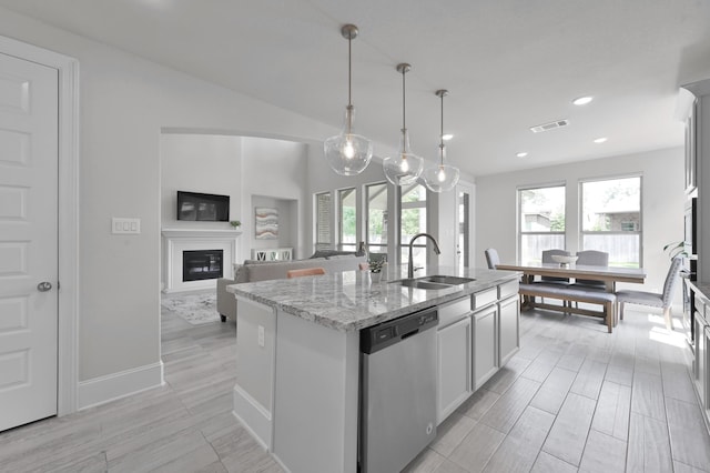 503 Woodsy Pine Ct, Conroe, TX 77304 - kitchen with stainless steel dishwasher, a sink, a center island with sink, light stone counters, and a glass covered fireplace