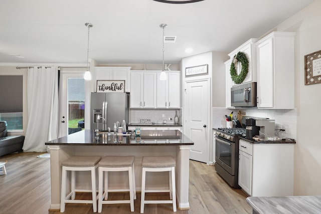 31110 Birch Mills Dr, Hockley, TX 77447 - kitchen with stainless steel appliances, backsplash, light wood-style flooring, white cabinetry, and an island with sink