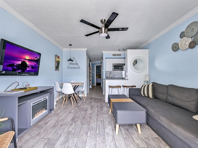 6300 Seawall Blvd Unit 3123, Galveston, TX 77551 - living room featuring a ceiling fan, crown molding, a glass covered fireplace, and light wood finished floors