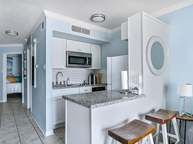 6300 Seawall Blvd Unit 3123, Galveston, TX 77551 - kitchen featuring stainless steel microwave, freestanding refrigerator, white cabinetry, a sink, and decorative backsplash