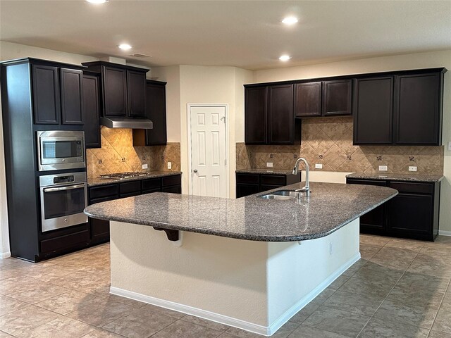 9314 Wheatfield Ln, Rosenberg, TX 77469 - kitchen featuring appliances with stainless steel finishes, under cabinet range hood, a sink, dark stone counters, and recessed lighting