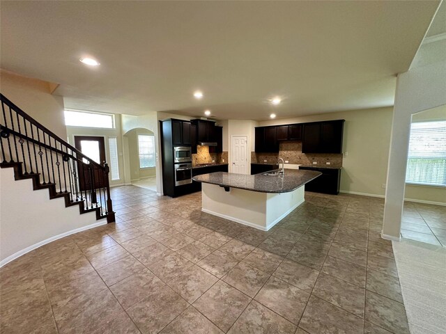 9314 Wheatfield Ln, Rosenberg, TX 77469 - kitchen with stainless steel appliances, backsplash, arched walkways, a center island with sink, and recessed lighting