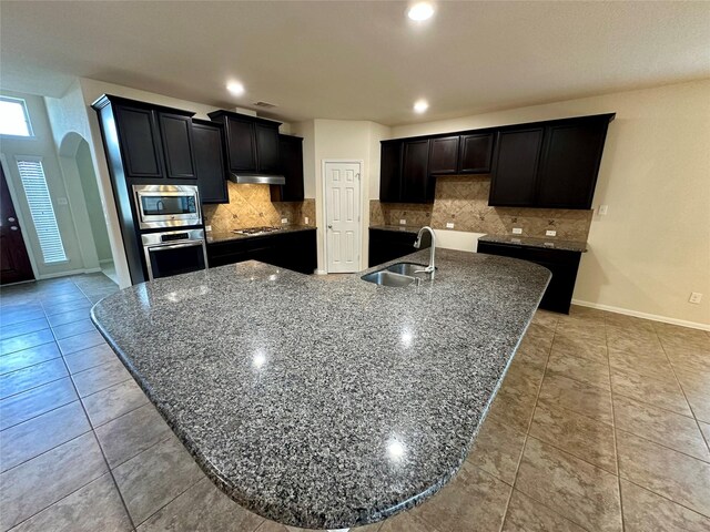 9314 Wheatfield Ln, Rosenberg, TX 77469 - kitchen featuring appliances with stainless steel finishes, a sink, a spacious island, baseboards, and under cabinet range hood