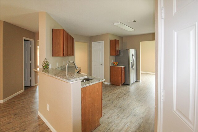 16726 Warbler Dr, Conroe, TX 77385 - kitchen featuring stainless steel fridge with ice dispenser, brown cabinetry, light wood-style floors, a peninsula, and baseboards