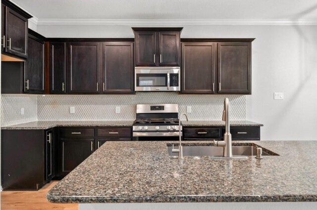 910 S Chamfer Way, Crosby, TX 77532 - kitchen with appliances with stainless steel finishes, a sink, dark stone counters, crown molding, and light wood-style floors