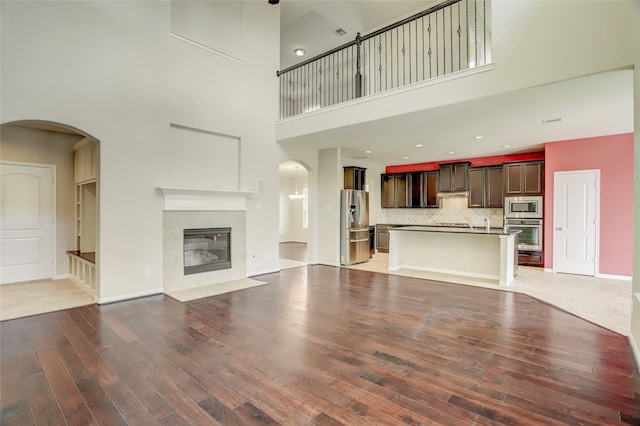 5402 Bending Branch Dr, Missouri City, TX 77459 - unfurnished living room featuring light wood-type flooring, a towering ceiling, arched walkways, a tiled fireplace, and baseboards