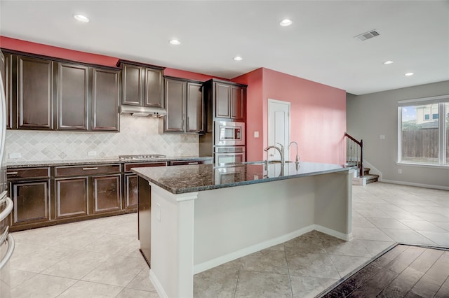 5402 Bending Branch Dr, Missouri City, TX 77459 - kitchen featuring appliances with stainless steel finishes, a sink, dark stone countertops, a kitchen island with sink, and tasteful backsplash