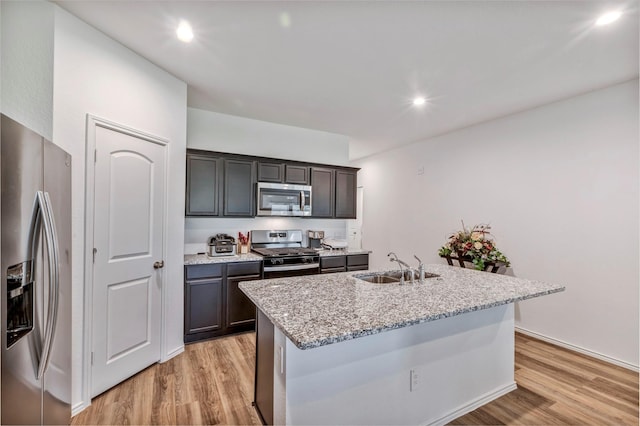 15007 Ashton Meadows Dr, New Caney, TX 77357 - kitchen with stainless steel appliances, a sink, light wood-style floors, light stone counters, and an island with sink