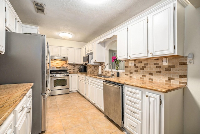 116 Whiting St, Galveston, TX 77550 - kitchen featuring stainless steel appliances, under cabinet range hood, a textured ceiling, backsplash, and white cabinetry