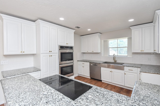 4618 Turf Valley Dr, Houston, TX 77084 - kitchen with stainless steel appliances, a sink, dark wood finished floors, white cabinets, and recessed lighting