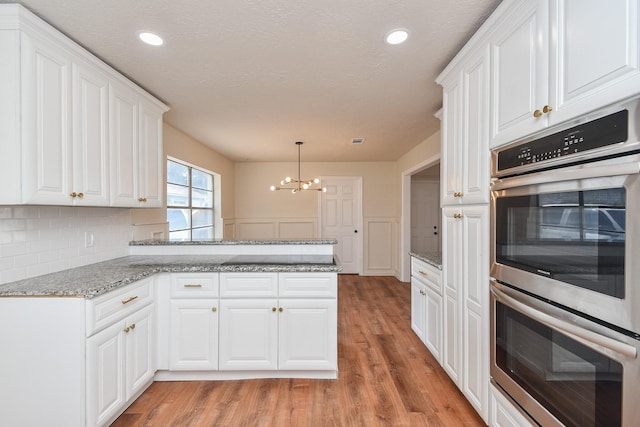 4618 Turf Valley Dr, Houston, TX 77084 - kitchen with double oven, light wood finished floors, a chandelier, a peninsula, and white cabinetry