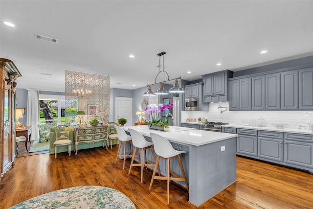 1819 Mill Creek Dr, Houston, TX 77008 - kitchen featuring gray cabinetry, stainless steel appliances, light countertops, an island with sink, and decorative backsplash