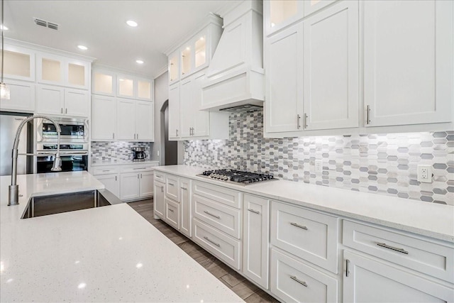 8105 Denali Dr, Corpus Christi, TX 78414 - kitchen with custom exhaust hood, a sink, white cabinetry, appliances with stainless steel finishes, and backsplash