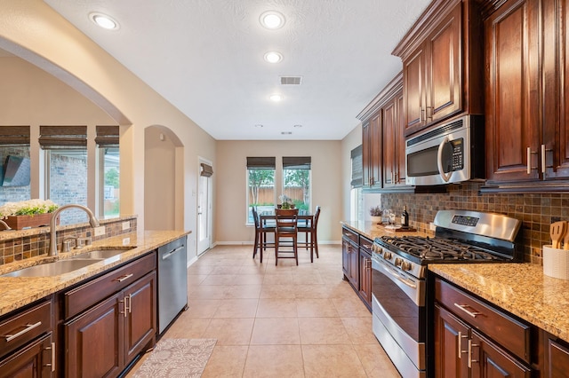4726 Ashley Hope Dr, Katy, TX 77494 - kitchen with stainless steel appliances, a sink, backsplash, arched walkways, and light stone countertops