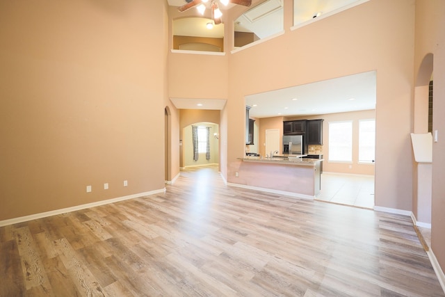 6707 Hunters Creek Ln, Baytown, TX 77521 - unfurnished living room with arched walkways, a ceiling fan, light wood-style flooring, baseboards, and a high ceiling